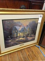 Full view of framed Thomas Kincade winter cottage print 'Blessings of Christmas' showing the ornate gold frame, matting, and snow scene with cottage and snowman at dusk.