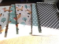 Photo of five folded towels with fox and tree print, and a checkered towel, arranged on a wooden surface in sunlight.