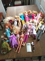 Photo of 27 dolls mostly Barbie and Barbie sized, showing worn condition and variety of outfits and styles