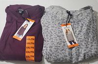Two folded Buffalo David Bitton ladies knit tops in purple and gray with tags and size XXL stickers visible.