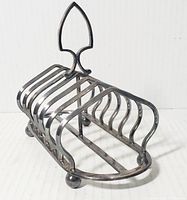 Front angle of vintage silver-tone toast holder with six slots to hold toast upright and decorative spear handle.