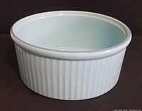 Photo of vintage turquoise ceramic souffle bowl showing exterior vertical ridges and round top rim, placed on black background