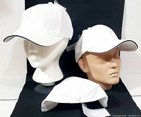 Three white fitted ball caps displayed on mannequin heads and lying down, showing the front and side views with midnight navy edging on the brim and tags attached.