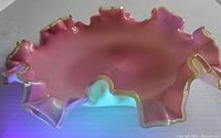 Top view showing pink glass bowl with ruffled gold-trimmed edges under natural light