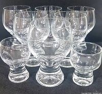 Six clear crystal goblets and two shot glasses with thick bases arranged on black fabric surface.