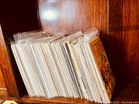 Photo showing a large collection of comic books in plastic protective sleeves, arranged vertically on a wooden shelf.