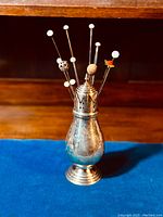 Overall view of silver-plated hatpin holder with eight hatpins inserted, showing height and decorative crown top.