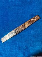 Top view of large sterling silver hair clip on blue background showing detailed engraved scrollwork