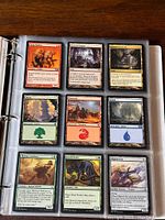 Binder open showing a page with nine Magic the Gathering cards in clear protective sleeves, depicting creatures, lands, and spell cards from the game.