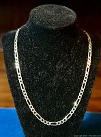 Figaro style sterling silver chain necklace displayed on black velvet bust form showing full length and link pattern.