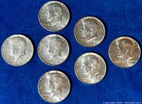 Six US Kennedy half-dollar coins arranged on blue background showing obverse portrait sides with years 1966, 1967 x3, 1968 x2, and 1969 visible.