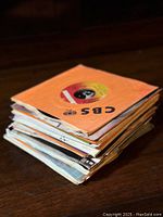 Stack of vintage 7-inch 45 RPM vinyl records showing CBS paper sleeves and various other sleeves stacked on a wooden surface.