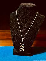 Full view of the necklace displayed on a black velvet bust stand showing the silver leaf pendant with multicolored gemstones and fine silver chain.