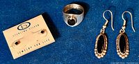 Photo of sterling silver ring with round onyx center, onyx stud earrings on card, and dangling oval onyx earrings, displayed on dark fabric