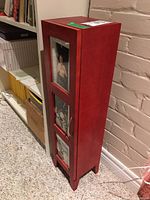 Left side angle of the red wooden display cabinet showing three glass panel doors and the cabinet's front profile.