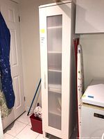 Front view of tall white cabinet with frosted glass door, closed.