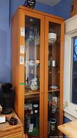 Full view of the tall manufactured wood cabinet with glass doors showing contents inside (contents not included in lot).