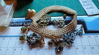 Assortment of costume jewelry laid out showing pearl collar necklace, brooches with rhinestones, and multiple pairs of screw back earrings.