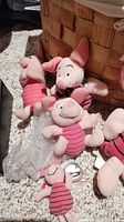 Five Disney Piglet plush toys varying in sizes, one with keychain, arranged on carpet near wicker basket