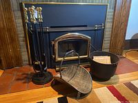 Photo showing complete fireplace tool set with poker, tongs, brush, shovel in stand, plus two log baskets in front of fireplace.