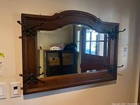 Front view of the large rectangular wall mirror featuring a dark wood frame and mounted black metal hooks.