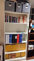 Front view of white Ikea Billy bookcase with books, binders, National Geographic magazines, and striped storage bins shown for scale and context.