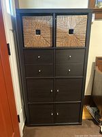 Front view of the Ikea laminated cabinet showing four wicker baskets on top and eight drawers below with metal knobs.