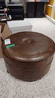 Front angle view of brown round vintage vinyl ottoman with central button tuft and visible wear.