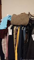 Various hanging clothing items including a brown knit wool sweater, coats, vests, and blouses in various colors hung on hangers.
