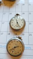 Two Westclox pocket watches laid on a calendar background showing dials, winding crowns, and subsidiary seconds dials.