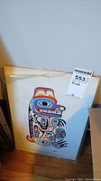 Unframed colorful print showing Indigenous-styled art with a large eye and colorful shapes, leaning against wall