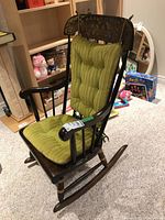 Side angle view of Nichols and Stone Co wooden rocking chair with green seat and backrest cushions, showing detailed wood carving and floral painted accents.