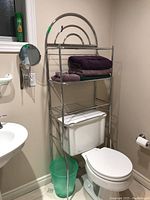 Metal bathroom shelving unit over toilet with folded towels on top shelf and wire rack shelves below.