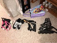 Photo of four skates on carpet including two pairs of ice skates and one pair of roller skates with a colorful bag nearby
