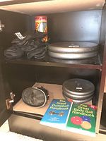 Shelf showing black padded hand protectors, metal weight plates (two 25 lbs and three 10 lbs), diving mask, and two exercise handbooks.
