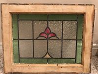 Full view of the rectangular stained glass panel in a wooden frame showing the overall design with a red floral pattern and green border pieces.