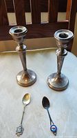 Both candle holders side by side with two spoons on cloth-covered surface