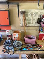 Overview of the tools on a wooden workbench including drills, saw, hand tools, axe, and a pink Rubbermaid storage bin