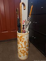 Image of ceramic umbrella stand filled with umbrellas and a walking cane against a red door and cabinetry.