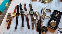 Overview of 9 assorted wristwatches with various band types and colors laid on calendar background.