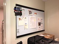 Full shot of the whiteboard with attached papers and accessories, showing the front view on a beige wall.