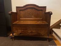 Front view of oak deacan's bench showing high backrest with panel and curved armrests. Seat in closed position reveals surface distressing.