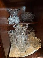 Glass and crystal items arranged on two buffet shelves, showing multiple bowls, vases, and small containers with cut designs.