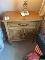 Front, angled view of the wood nightstand showing top, drawer, and door details with lamp on top.