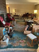 Wide view of the large wool area rug with floral design and fringe, laid out in a living room with furniture and boxes on top.