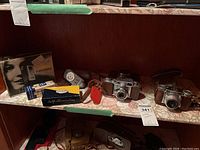 Photo of shelf with two vintage cameras, Mecablitz flash box, light meter, and viewer box.