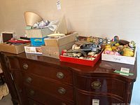 Wide shot showing multiple boxes containing various vintage toys including a model airplane, toy car, lamp, and plush toys on a wooden cabinet
