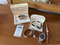 Overview photo showing six vintage men's and women's watches, including two watches in original cases (one Glycine and one white case). Various metal bands and a decorative floral enamel bracelet included.