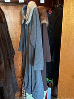 Two vintage wool coats with fur collars hanging in closet, one grey and one brown, medium size.