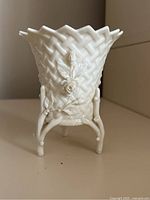 Front view of the white Belleek porcelain triangular footed spill vase with applied floral decorations and basket weave texture.